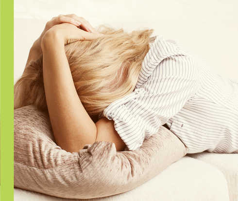 Urtikaria: Depressionen und Schlafstörungen Eine Frau liegt mit ihrem Gesicht in einem Kissen und hält sich den Kopf.