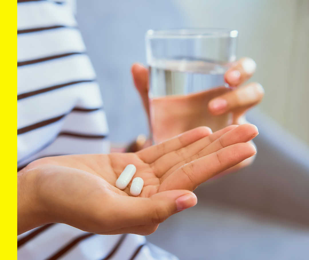 Akne inversa: Systemische Medikamente Eine Person hält ein Glas Wasser und zwei Tabletten in der Hand.
