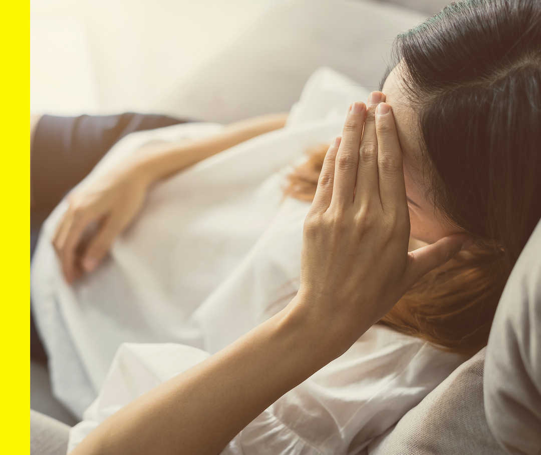 Akne inversa: Schmerzen Eine Patientin liegt auf dem Sofa und fasst sich an die Stirn.