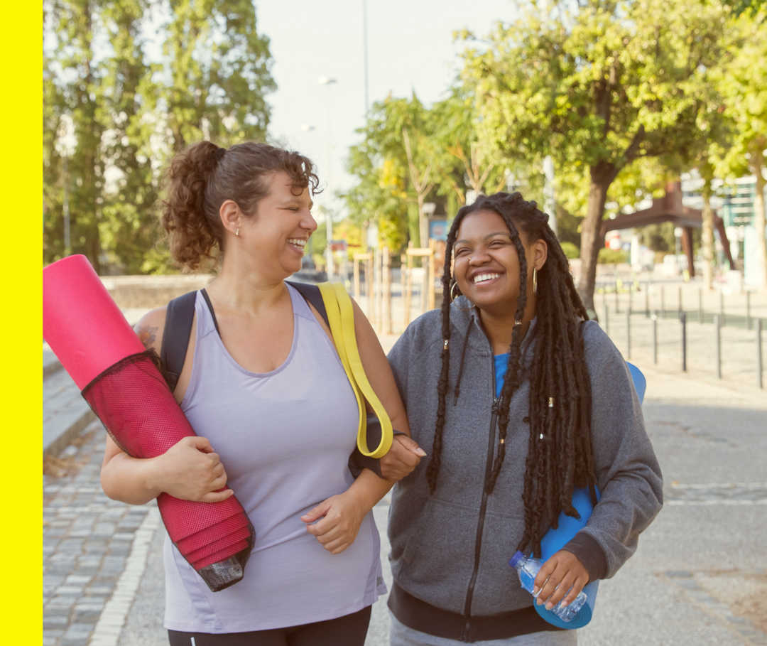 Akne inversa: Gewichtsreduktion Zwei Freundinnen in Sportkleidung mit Yogamatten.