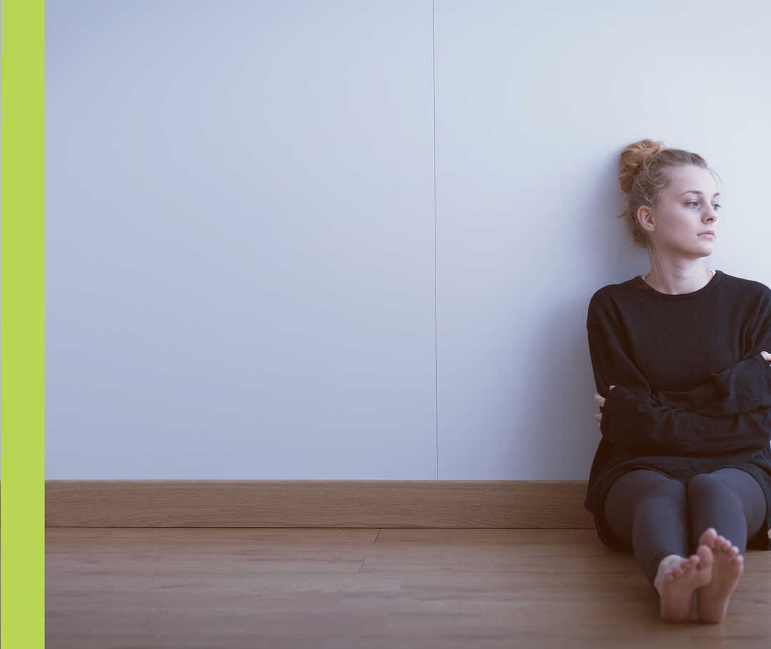 Nesselsucht-Symptome: Depressionen Eine Frau sitzt auf dem Boden mit angelehnten Rücken zur Wand.