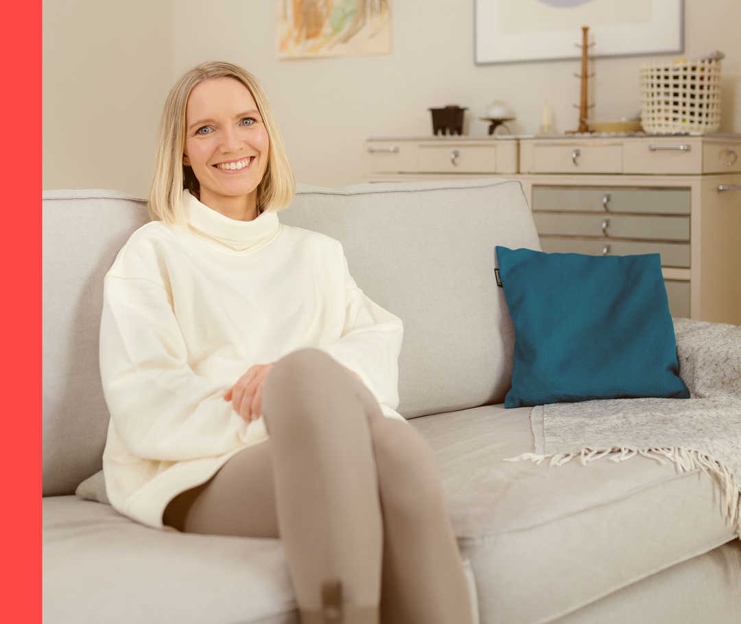 Psoriasis-Patientenblog: Anna Lenas HAUTgeschichte Anna Lena sitzt lächelnd auf einem Sofa und schaut in die Kamera.