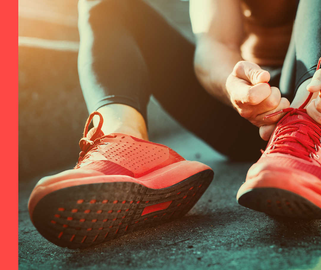 Hautwende: Psoriasis und Gründe für Sport Eine Person bindet sich im Sitzen die Schnürsenkel ihrer roten Sportschuhe.