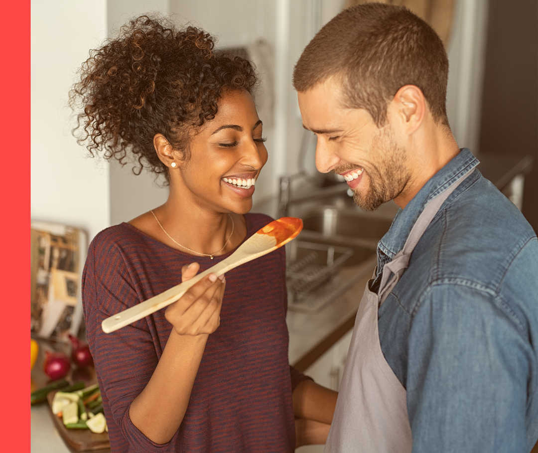 Psoriasis: Lecker – was deine Haut liebt Paar kocht gemeinsam, Mann probiert vom Löffel mit Sauce.