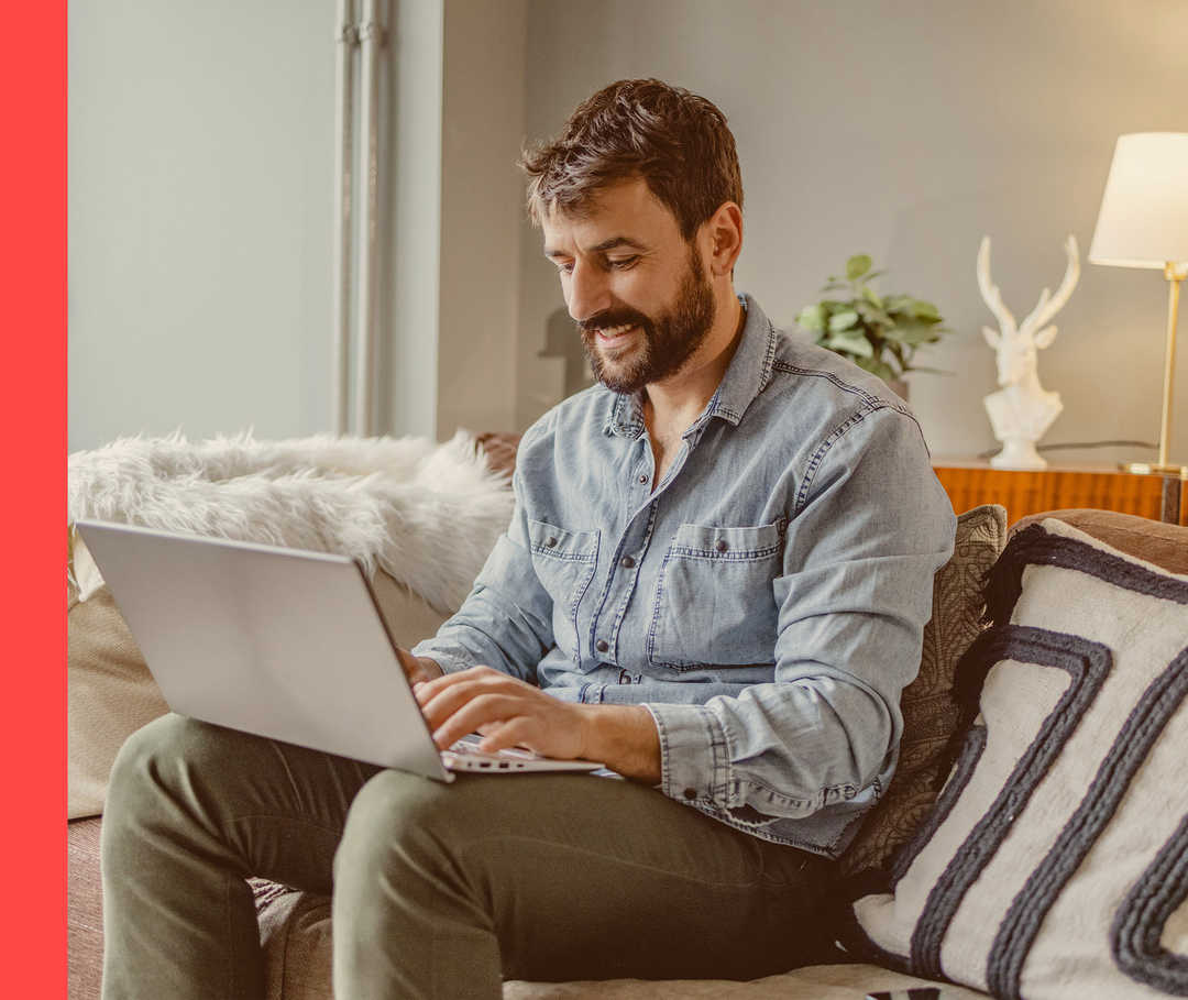 Videos Psoriasis Ein Mann sitzt mit seinem Laptop auf einem Sofa.