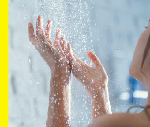 Eine junge Frau hält ihre Hände unter den laufenden Wasserhahn ihrer Dusche.
