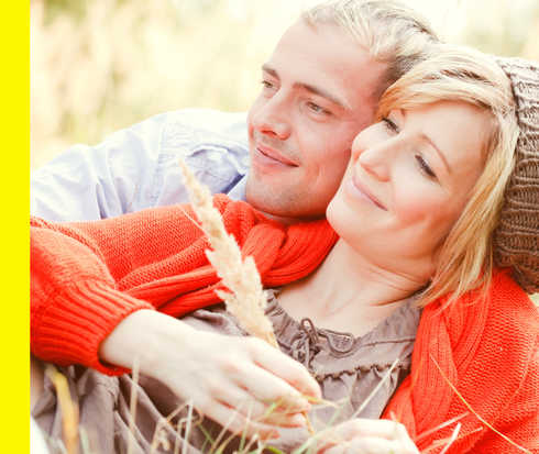 Ein Mann und eine Frau liegen lächelnd Arm in Arm auf einer Wiese.