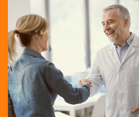 Eine lachende Person im weißen Kittel schüttelt einer anderen Person die Hand. 