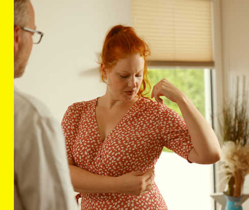 Eine Patientin fasst sich an ihre Rippe 