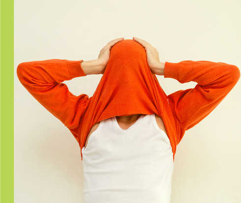 Ein Mann zieht sich einen roten Pullover über sein Gesicht und hält sich den Kopf.