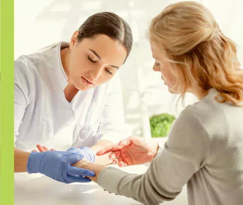 Eine Frau in weißem Kittel untersucht den linken Arm einer anderen Frau.