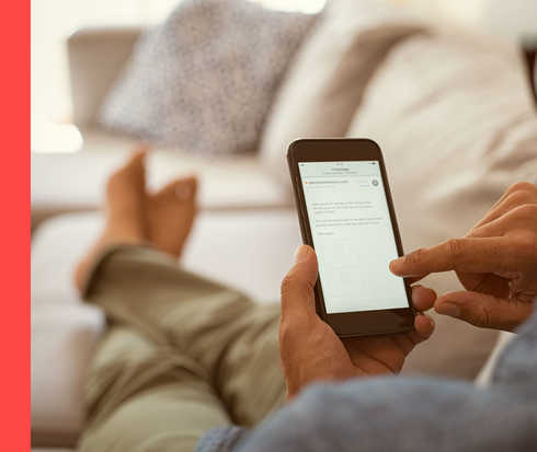 Bildausschnitt einer Person, die auf einem Sofa sitzt und ein Smartphone in der Hand hält.