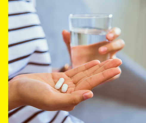 Eine Patientin hält ein Glas Wasser und zwei Tabletten in der Hand.