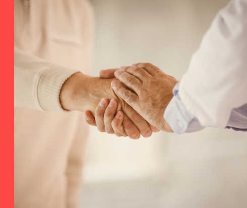 Nahaufnahme von einer Person im weißen Kittel, die die Hand einer anderen Person hält.