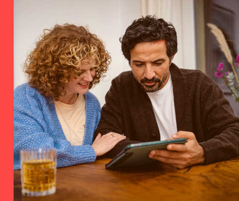 Ein Mann und eine Frau sitzen an einem Tisch und schauen auf einen Tablet-PC.