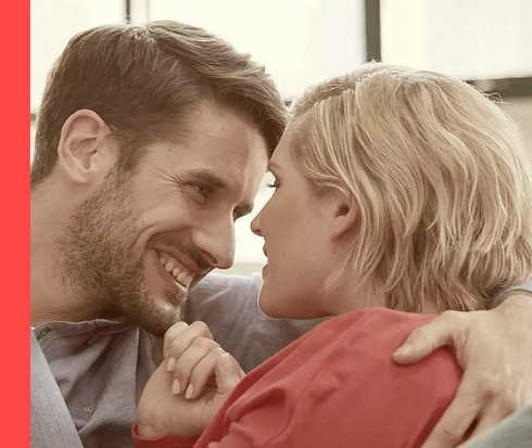 Ein dunkelhaariger Mann hält eine blonde Frau im Arm und lächelt sie an.