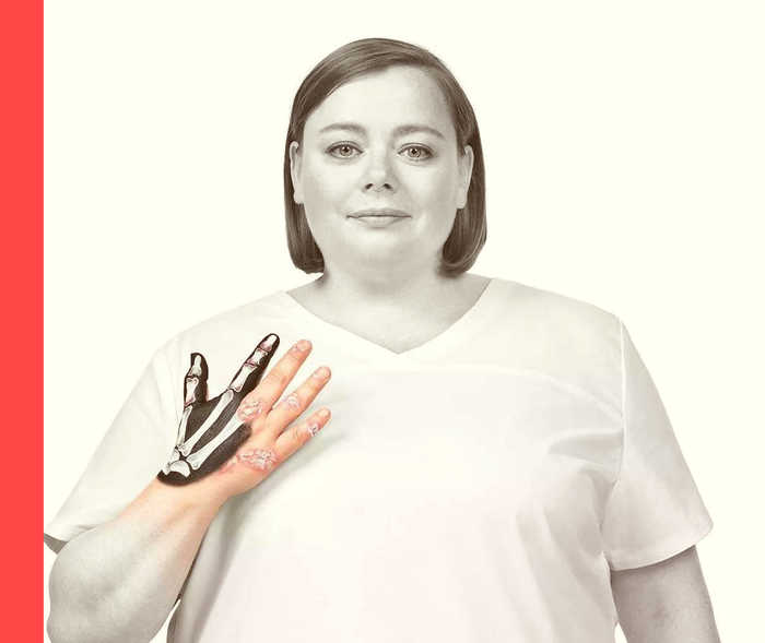 Eine Frau in einem weißen T-Shirt hält ihre rechte Hand hoch, in der symbolisch mehrere Fingerknochen zu erkennen sind.
