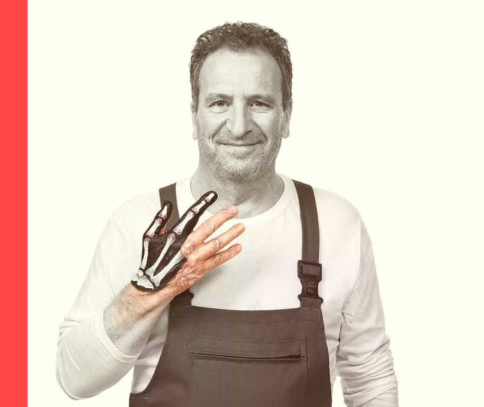 Ein Mann im Blaumann hält seine rechte Hand hoch und spreizt die Finger. Zwei Finger sind grafisch als Knochen abgebildet.