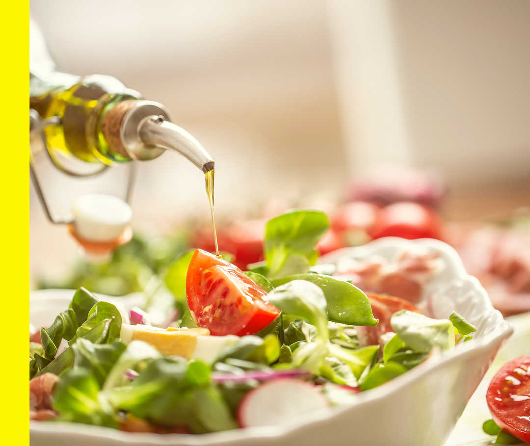Aus einer Flasche wird Öl auf einen Salat gegossen.