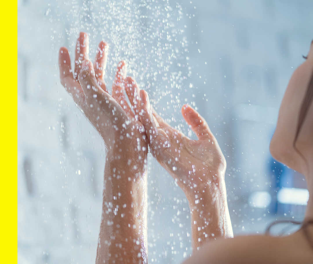 Eine junge Frau hält ihre Hände unter den laufenden Wasserhahn ihrer Dusche.