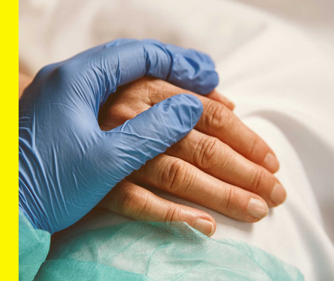 Nahaufnahme einer Hand im blauen OP-Handschuh, die die Hand einer anderen Person berührt.