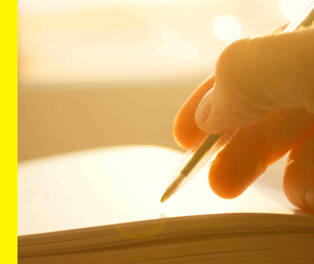 Offenes Buch mit leerer Seite und eine Hand, die im goldenen Licht einen Stift hält. 