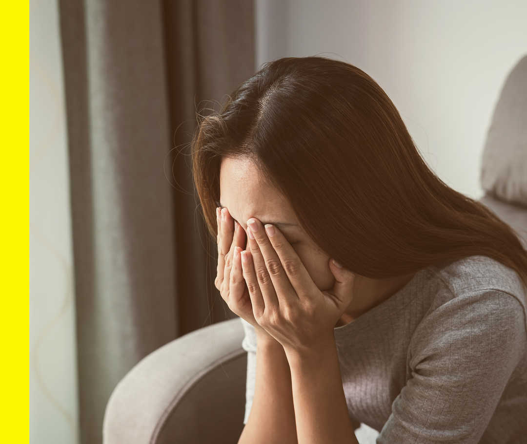 Eine sitzende Person bedeckt mit beiden Händen ihr Gesicht.