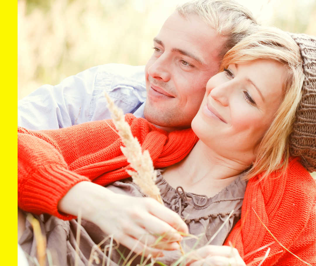 Ein Mann und eine Frau liegen lächelnd Arm in Arm auf einer Wiese.
