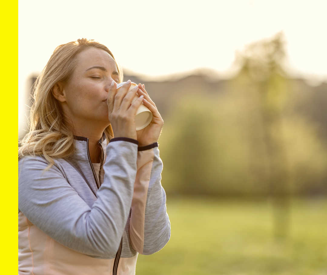 Eine Frau in Sportkleidung trinkt aus einem To-go-Becher.