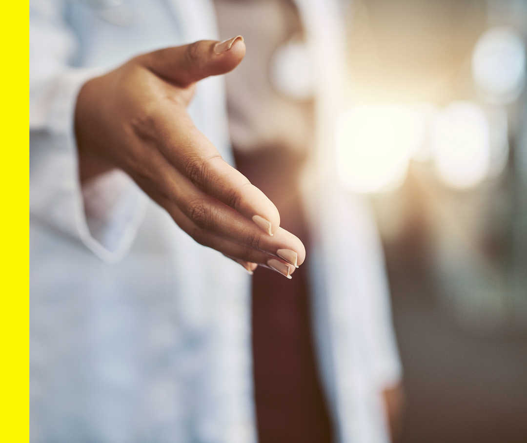 Eine Frau in einem weißen Arztkittel reicht ihre rechte Hand.