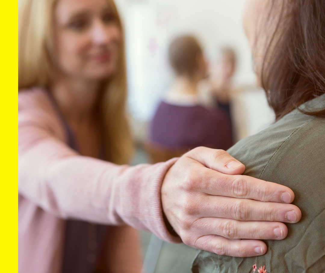 Nahaufnahme einer Hand, die auf der Schulter einer anderen Person liegt.