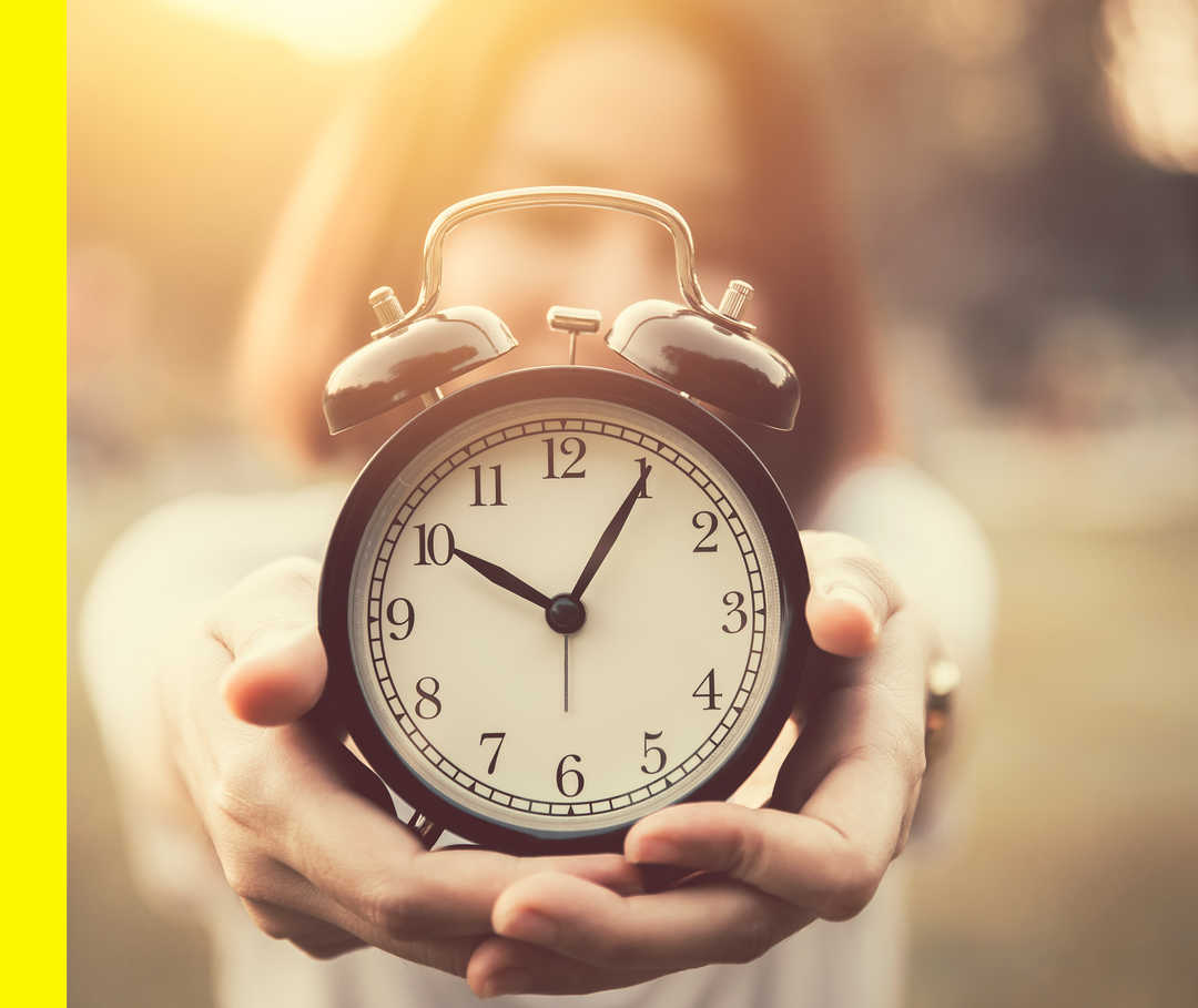 Nahaufnahme von zwei Händen, die einen altmodischen Wecker in die Kamera halten.