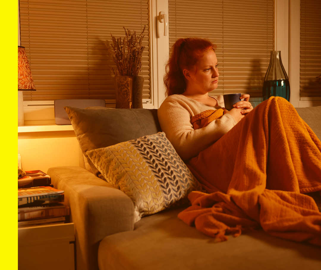 Eine Frau sitzt auf Ihrer Couch mit einer Decke und hat Schmerzen