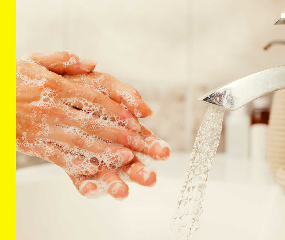 Eine Person seift sich ihre Hände unter einem Wasserhahn ein.