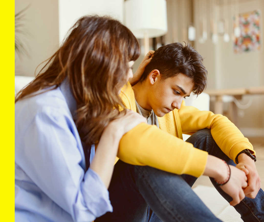 Eine Person berührt eine junge Person, die am Boden sitzt.