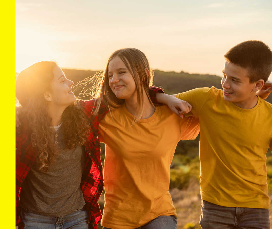 Vier junge Menschen stehen Arm in Arm in einer Reihe im Freien und lächeln.
