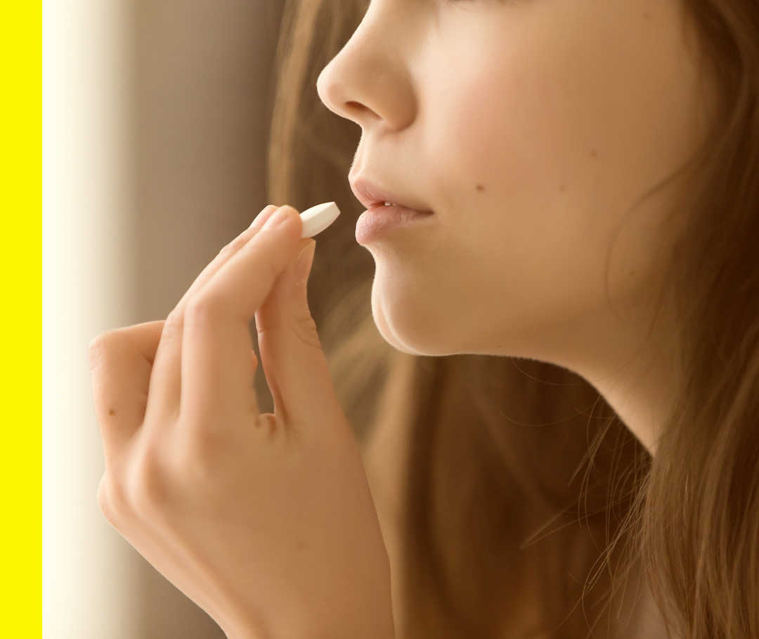 Nahaufnahme einer Hand, die eine Tablette zum Mund einer Person führt.