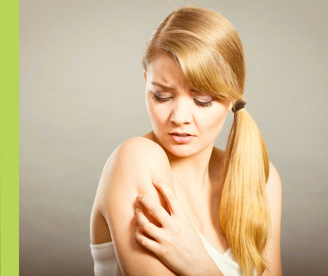 Eine Frau kratzt ihre rechte Schulter.