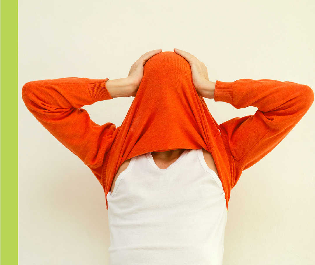 Ein Mann zieht sich einen roten Pullover über sein Gesicht und hält sich den Kopf.