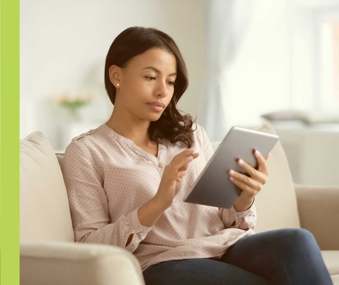 Eine Frau sitzt auf einem Sofa und schaut auf ein Tablet.