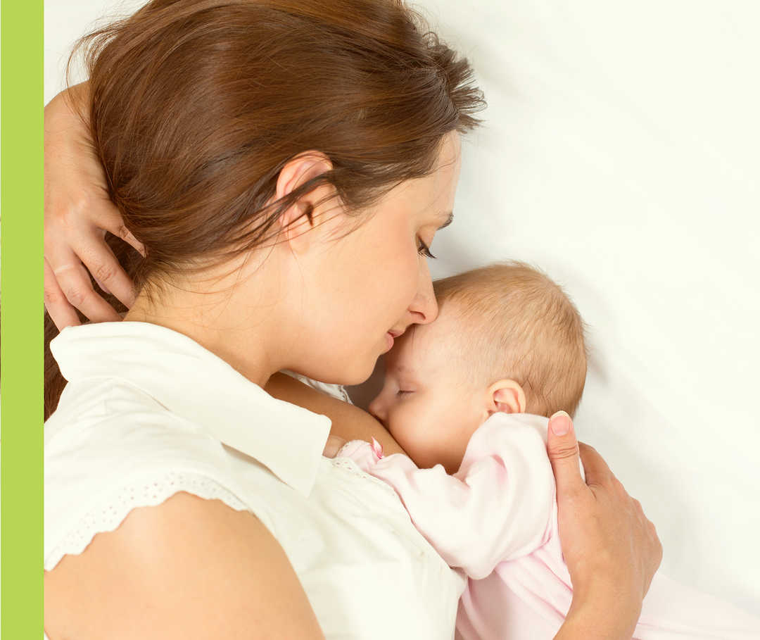 Eine liegende Frau hält ein Baby im Arm.