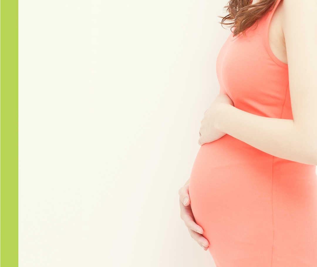 Eine schwangere Frau in einem roten Kleid hält sich den Bauch.