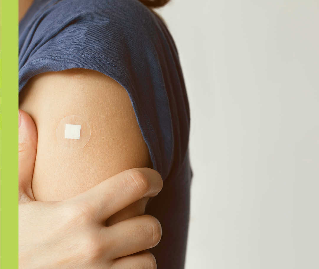 Eine Person hält sich den Oberarm, auf dem ein Pflaster klebt.