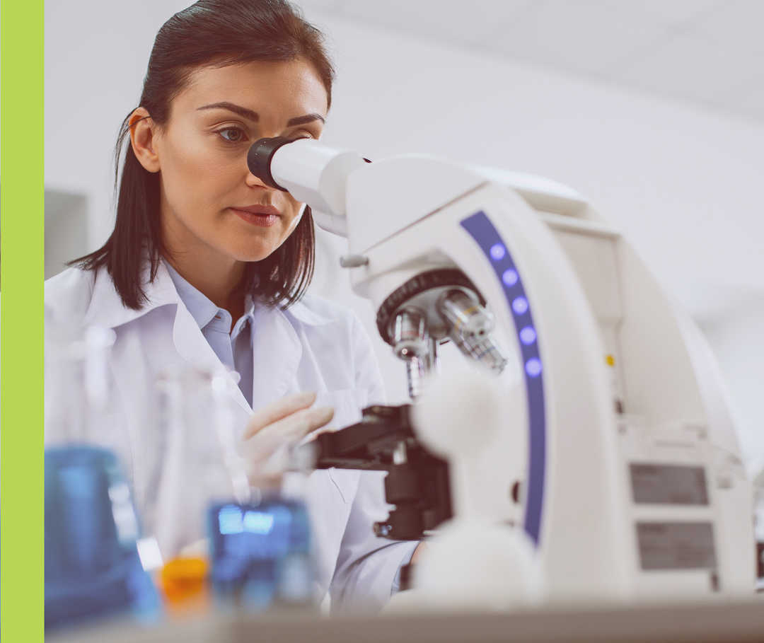 Eine Frau im weißen Kittel schaut in ein Mikroskop.