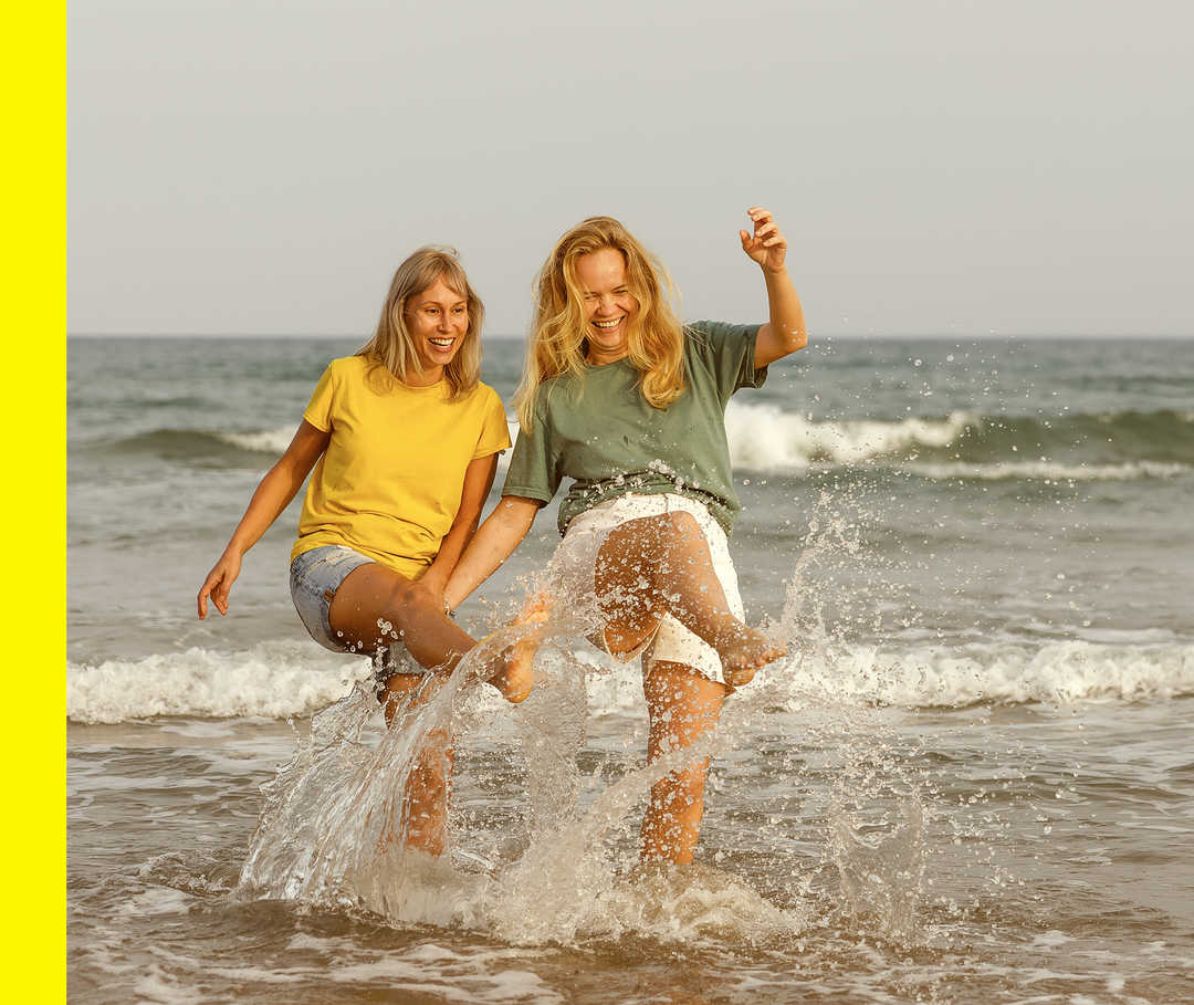 Zwei Personen lachen zusammen im Meer und spritzen mit Wasser.