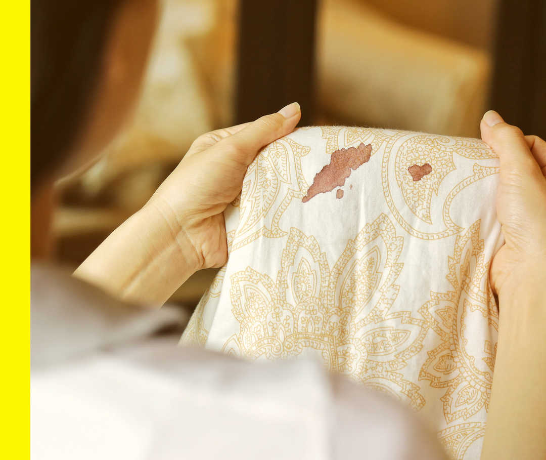 Eine Person hält ein Kleidungsstück mit rötlichen Flecken hoch.