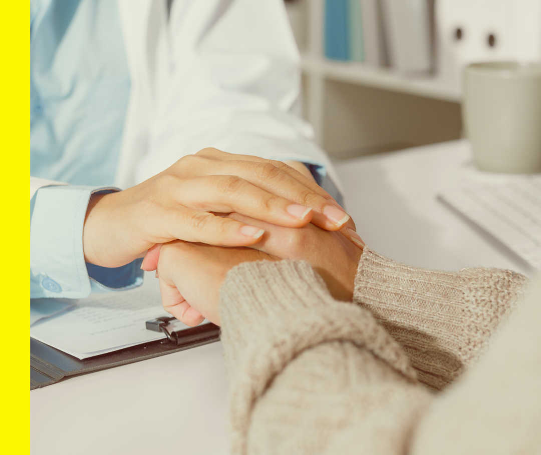 Nahaufnahme von den Händen einer Person im weißen Kittel, die die Hände einer anderen Person hält.