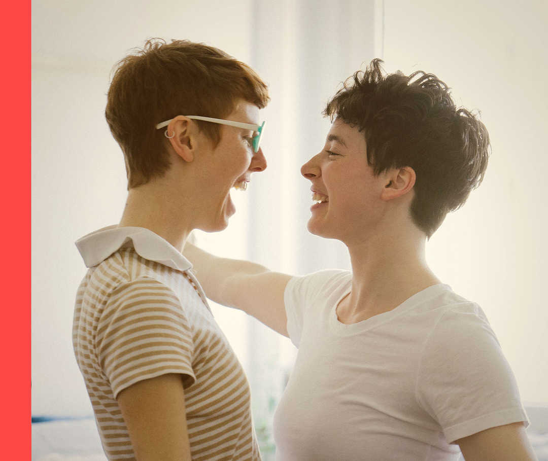 Das Bild zeigt zwei Frauen, die sich gegenüberstehen und lächeln.