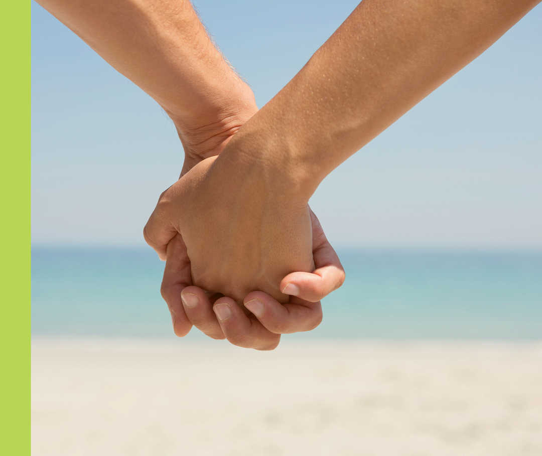 Nahaufnahme von zwei Personen, die am Strand Händchen halten.