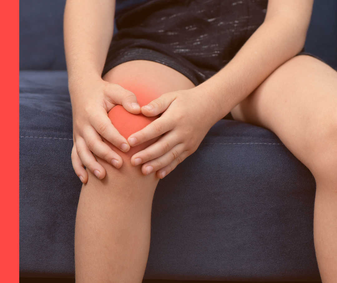 Kind hält beide Hände ans rechte Bein unterhalb seines roten Knies.